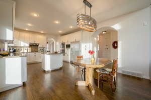 Dining space with arched walkways, dark wood floors, and recessed lighting