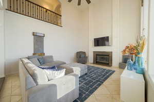 Living room with a towering ceiling, a fireplace with flush hearth, light tile patterned floors, and a ceiling fan