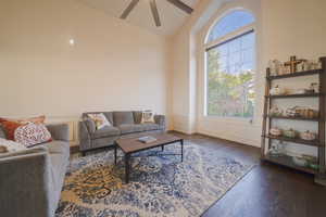Living room with dark wood floors, wainscoting, a ceiling fan, high vaulted ceiling, and a decorative wall
