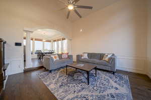 Living area with a decorative wall, wainscoting, arched walkways, dark wood flooring, and decorative columns