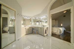 Ensuite bathroom featuring light marble finish floors, double vanity, high vaulted ceiling, and a ceiling fan