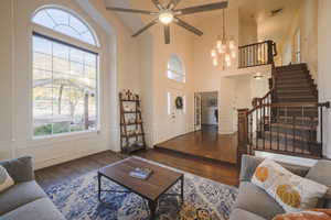 Living room with dark wood floors, a decorative wall, a wainscoted wall, stairway, and ceiling fan