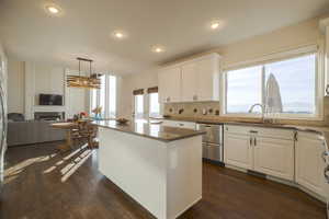 Kitchen featuring a kitchen island, dark stone countertops, backsplash, white cabinets, and decorative light fixtures