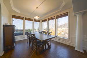 Dining space featuring decorative columns, crown molding, dark wood floors, wainscoting, and a decorative wall