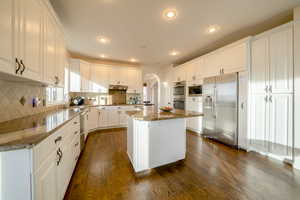 Kitchen featuring white cabinetry, dark wood floors, arched walkways, stainless steel appliances, and light stone countertops