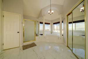 Full bath with a garden tub, a shower stall, marble look tiles, vaulted ceiling, and a chandelier