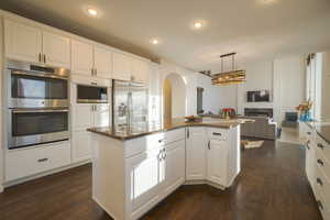 Kitchen featuring stainless steel appliances, white cabinetry, arched walkways, dark stone countertops, and recessed lighting
