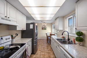 Kitchen with white appliances, white cabinetry, a chandelier, and under cabinet range hood