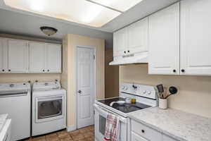 Kitchen featuring white electric range oven, white cabinetry, under cabinet range hood, dark tile patterned floors, and separate washer and dryer