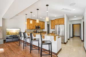 Kitchen with decorative backsplash, a kitchen breakfast bar, a peninsula, appliances with stainless steel finishes, and pendant lighting