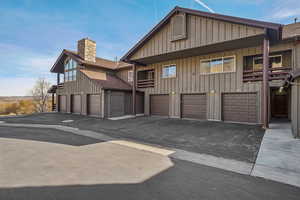 View of front of home with board and batten siding, an attached garage, asphalt driveway, and a chimney