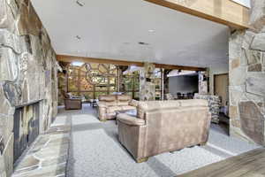 Common area featuring a stone fireplace, carpet floors, and beam ceiling