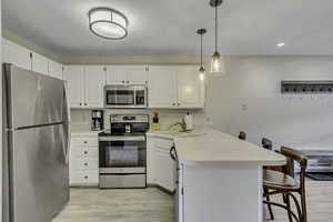 Kitchen featuring stainless steel appliances, a breakfast bar, light countertops, decorative light fixtures, and white cabinets