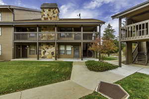 Rear view of house featuring stone siding, a yard, stairway, a chimney, and a shingled roof