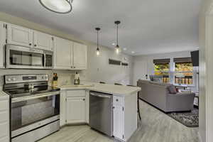 Kitchen with appliances with stainless steel finishes, a peninsula, white cabinetry, light countertops, and recessed lighting