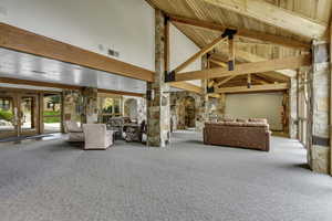 Common area with carpet flooring, high vaulted ceiling, arched walkways, and a wooden ceiling with exposed beams