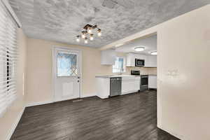Kitchen featuring white cabinets, stainless steel appliances, light countertops, dark wood-type flooring, and a chandelier