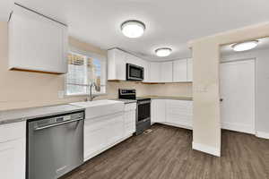 Kitchen featuring appliances with stainless steel finishes, white cabinets, dark wood-type flooring, and light stone countertops