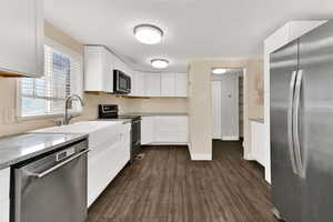 Kitchen featuring stainless steel appliances, white cabinets, dark wood-style flooring, and light stone counters