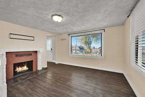 Unfurnished living room with dark wood finished floors, healthy amount of natural light, a fireplace, and a textured ceiling