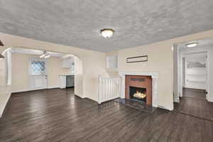 Unfurnished living room featuring dark wood-style floors, a fireplace, arched walkways, a textured ceiling, and a chandelier