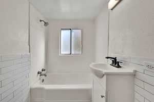 Full bath with tile walls, a textured wall, vanity,  shower combination, and a wainscoted wall