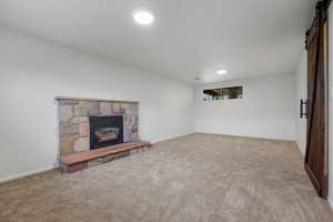 Unfurnished living room with a barn door, a stone fireplace, carpet floors, and recessed lighting