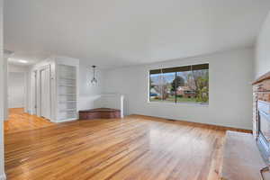 Unfurnished living room featuring light wood-style floors, a brick fireplace, and built in shelves