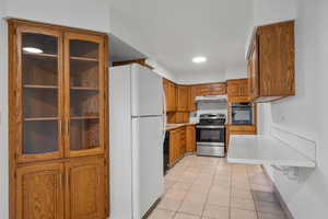 Kitchen with brown cabinetry, stainless steel appliances, light tile patterned floors, light countertops, and recessed lighting