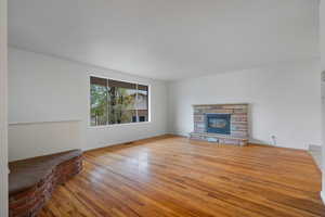 Unfurnished living room featuring light wood-style flooring and a stone fireplace