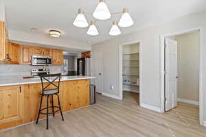 Kitchen featuring hanging light fixtures, a peninsula, a breakfast bar, appliances with stainless steel finishes, and light wood-style floors