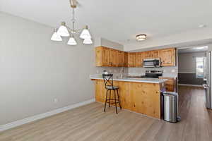 Kitchen featuring decorative light fixtures, a breakfast bar area, appliances with stainless steel finishes, a peninsula, and light wood-type flooring