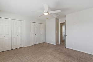 Unfurnished bedroom with two closets, carpet, and a ceiling fan