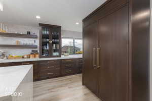 Kitchen with open shelves, dark brown cabinets, light stone counters, light wood-style flooring, and recessed lighting