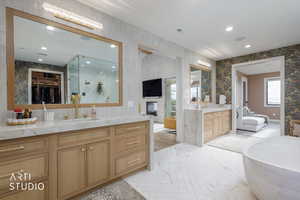 Bathroom with ensuite bathroom, a spacious closet, wallpapered walls, a fireplace, and two vanities