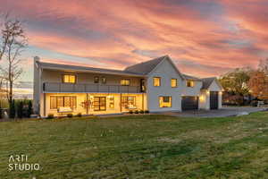Front of property at dusk featuring a yard, a chimney, a balcony, driveway, and an attached garage