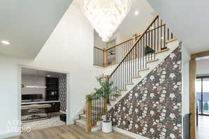 Entry stairs with recessed lighting, wood finished floors, a towering ceiling, and a chandelier