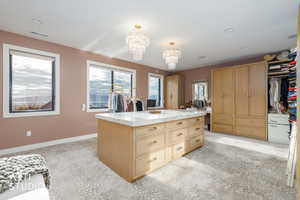 Large island featuring light brown cabinets, a chandelier, pendant lighting, light stone countertops, and a kitchen island