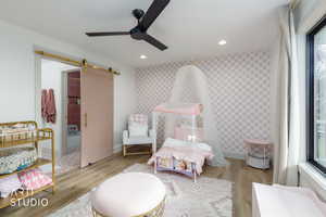 Bedroom featuring a barn door, wood finished floors, a ceiling fan, ensuite bath, and recessed lighting