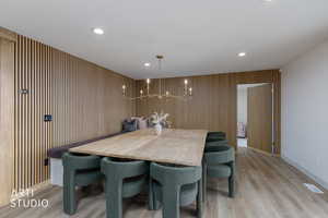Dining area with light wood finished floors, a chandelier, recessed lighting, and wood walls