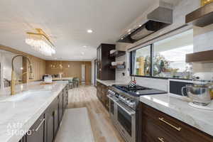 Kitchen featuring light stone countertops, range with two ovens, dark brown cabinets, open shelves, and light wood-style floors