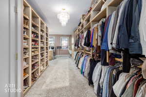 Walk in closet with light colored carpet and a chandelier