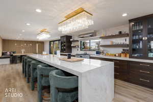 Kitchen with open shelves, dark brown cabinets, a kitchen breakfast bar, recessed lighting, and light stone countertops