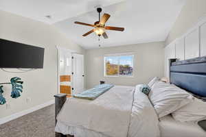 Carpeted bedroom featuring vaulted ceiling, a ceiling fan, and ensuite bath