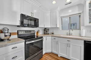 Kitchen featuring black appliances, white cabinetry, light wood-style flooring, recessed lighting, and light stone countertops