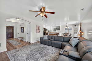 Living room featuring wood finished floors, ceiling fan, arched walkways, and a chandelier