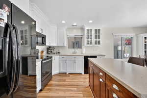 Kitchen featuring glass insert cabinets, black appliances, white cabinets, light wood-type flooring, and recessed lighting