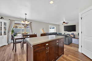 Kitchen with pendant lighting, a kitchen island, light wood-style floors, open floor plan, and dark brown cabinets