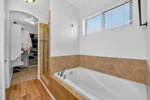 Full bath with light wood-type flooring, a shower stall, a garden tub, and a spacious closet
