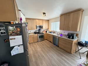 Kitchen featuring stainless steel appliances, light countertops, vaulted ceiling, light wood finished floors, and light brown cabinets